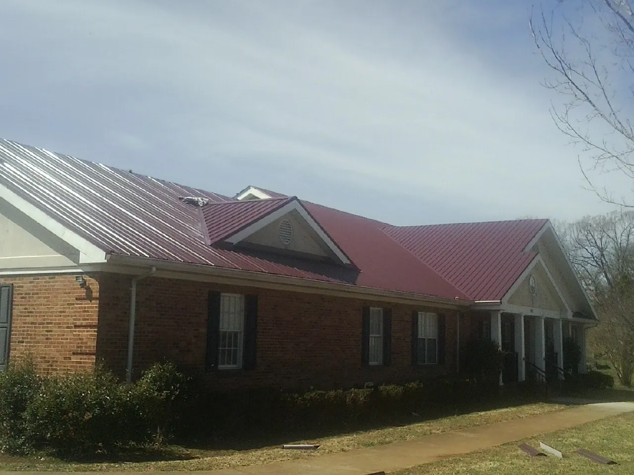 Red metal roof with gabled entries on a long brick building, from a Hail Damage Roof Repair job in Sauquoit