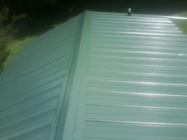 New green metal panels meeting at the ridge of a roof — Flat Roof Repair work by our crew in Sauquoit