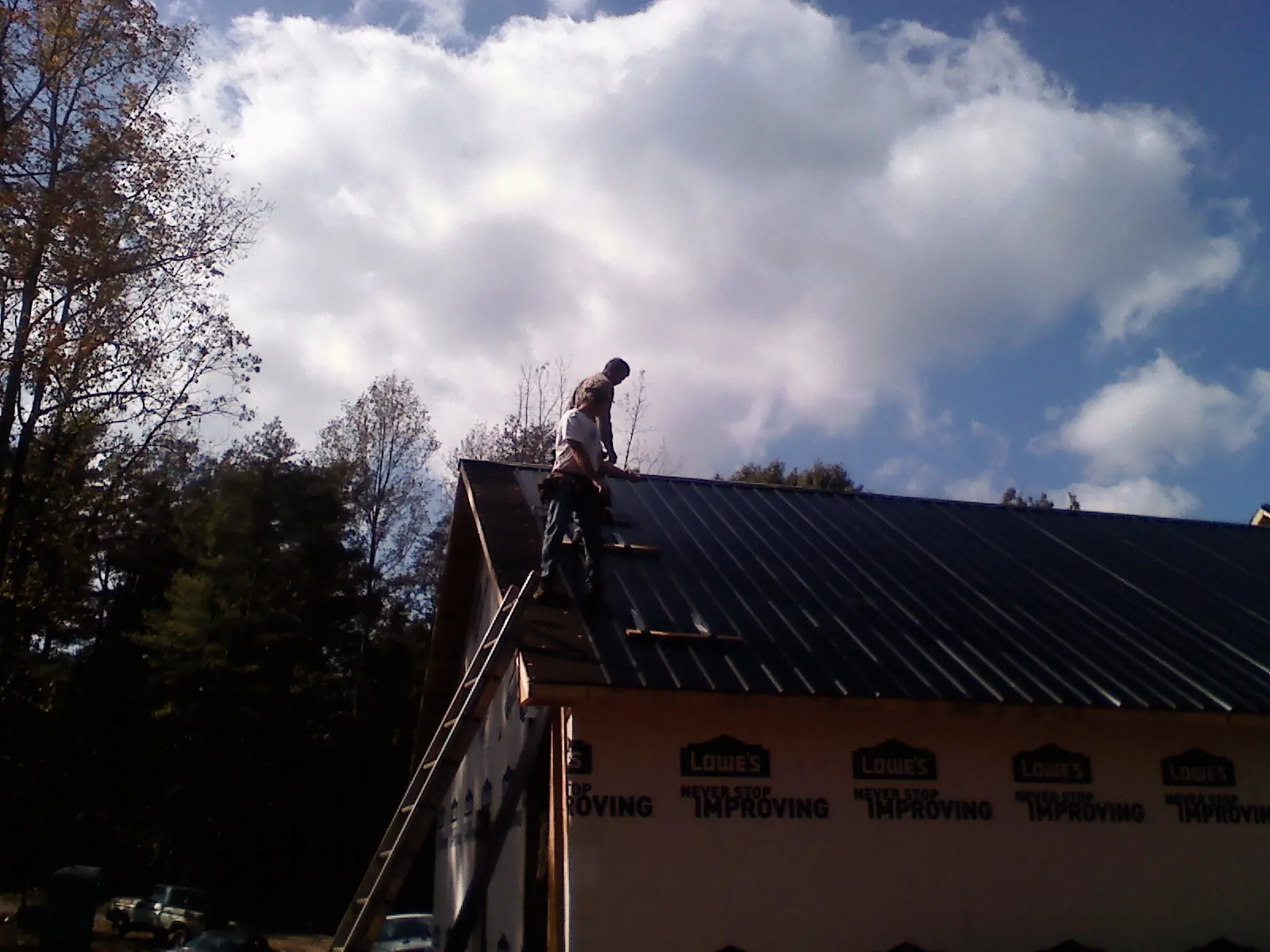 Roofer fastening dark metal panels high against a cloudy sky, from a Roof Inspection job in Sauquoit
