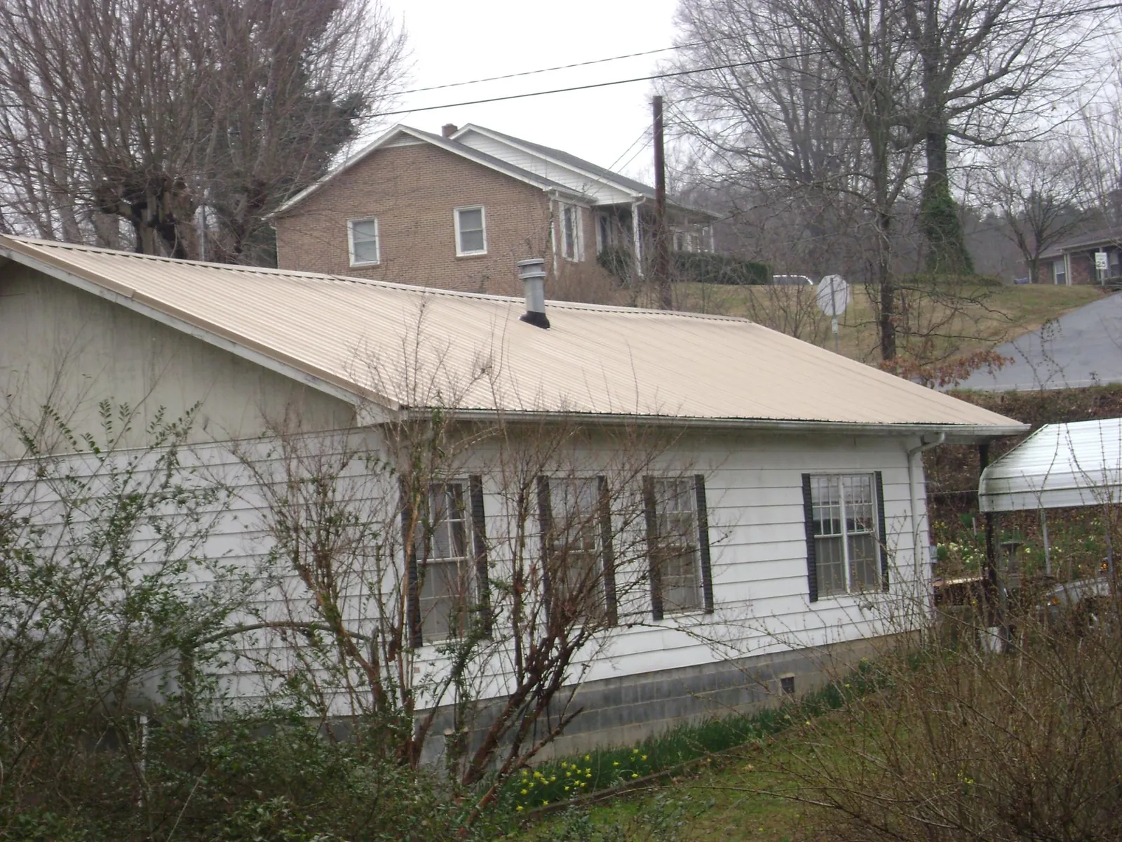 Tan metal roof on a white sided house set into a hillside — Commercial Roofing by Roofing Brothers in Sauquoit